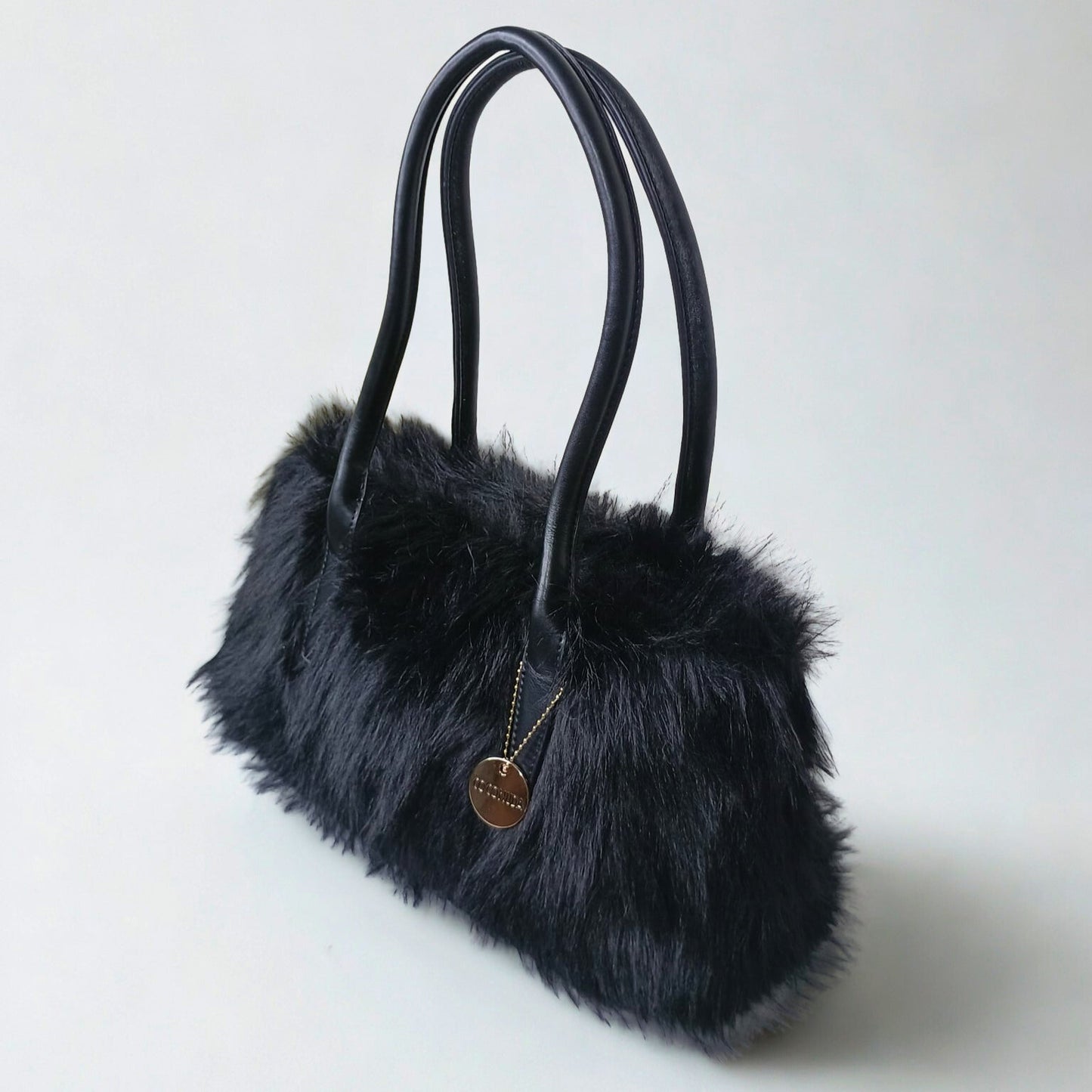 Black fur handbag with a gold tag on a light gray background