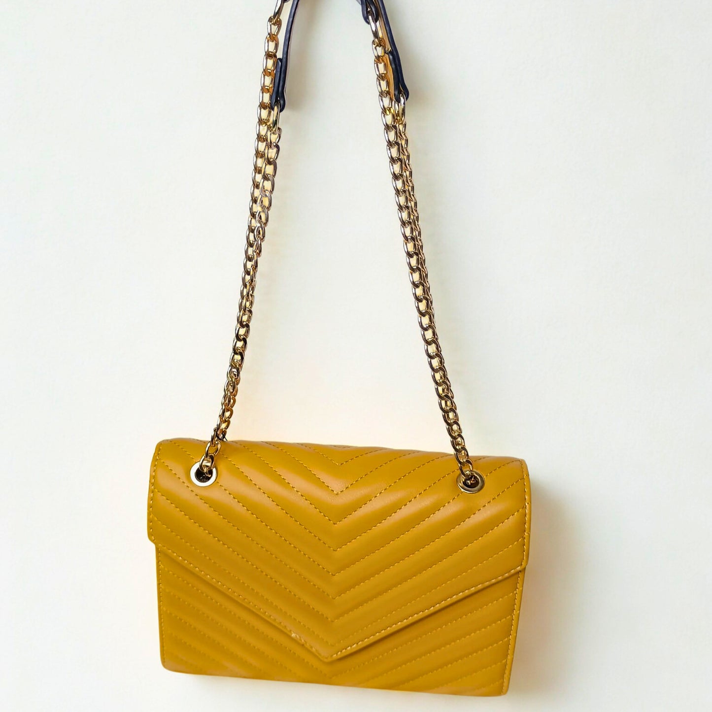 Yellow handbag with a gold chain strap on a white background