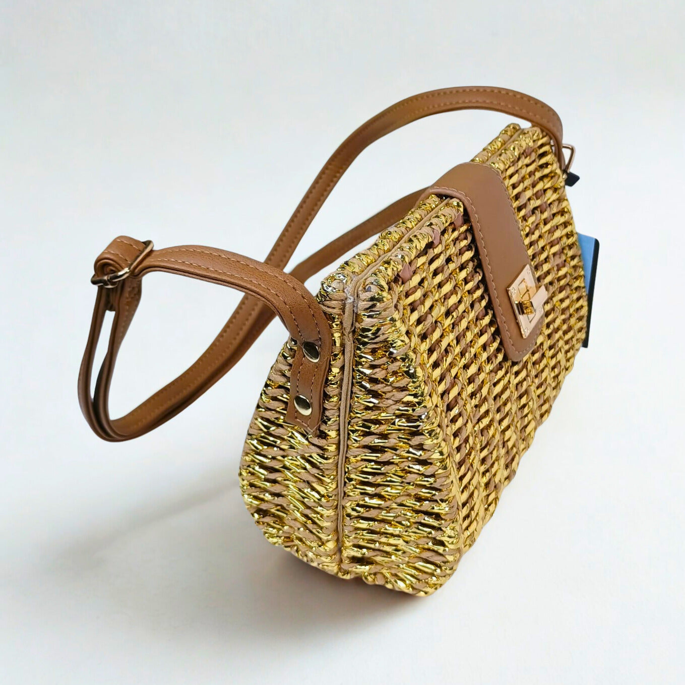 Woven straw handbag with brown leather strap on a white background