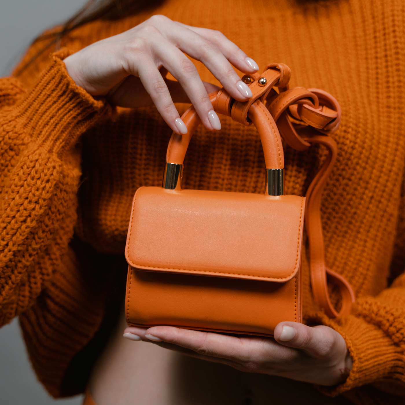 Person holding an orange handbag with matching sweater