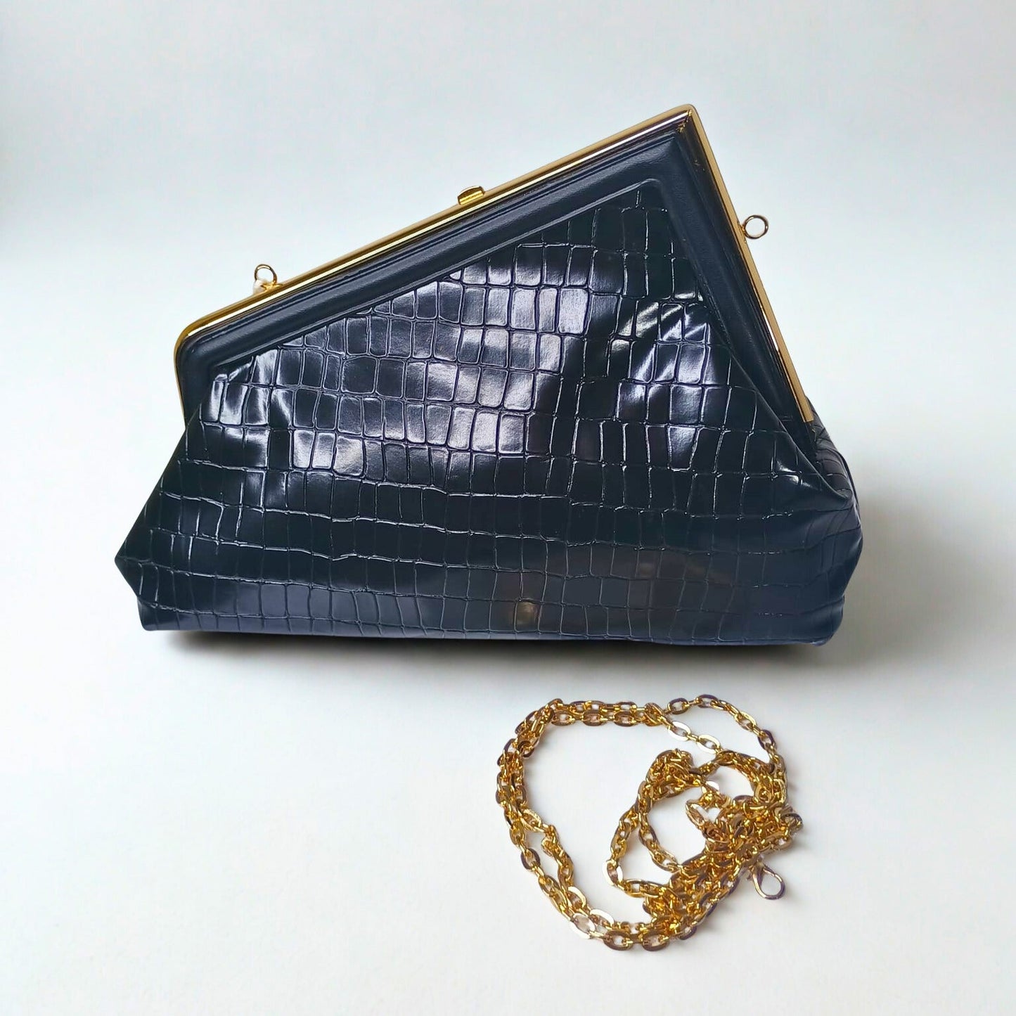 Navy blue crocodile skin handbag with gold chain on a white background
