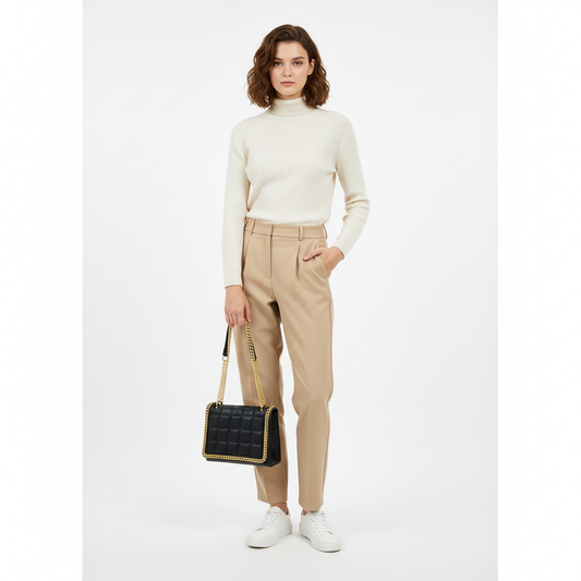 Woman wearing a white turtleneck, beige pants, and white shoes, holding a black handbag on a white background.