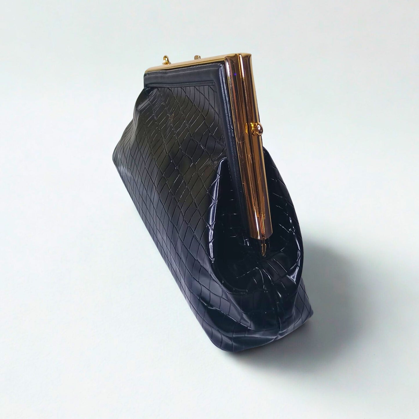 Black textured clutch bag with gold frame on a light gray background