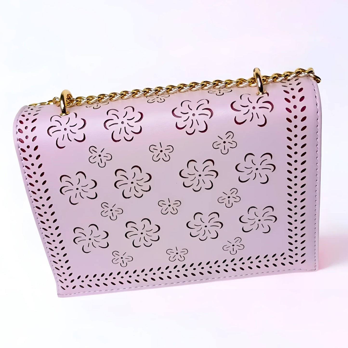 Pink handbag with floral cut-out design and gold chain strap on a white background