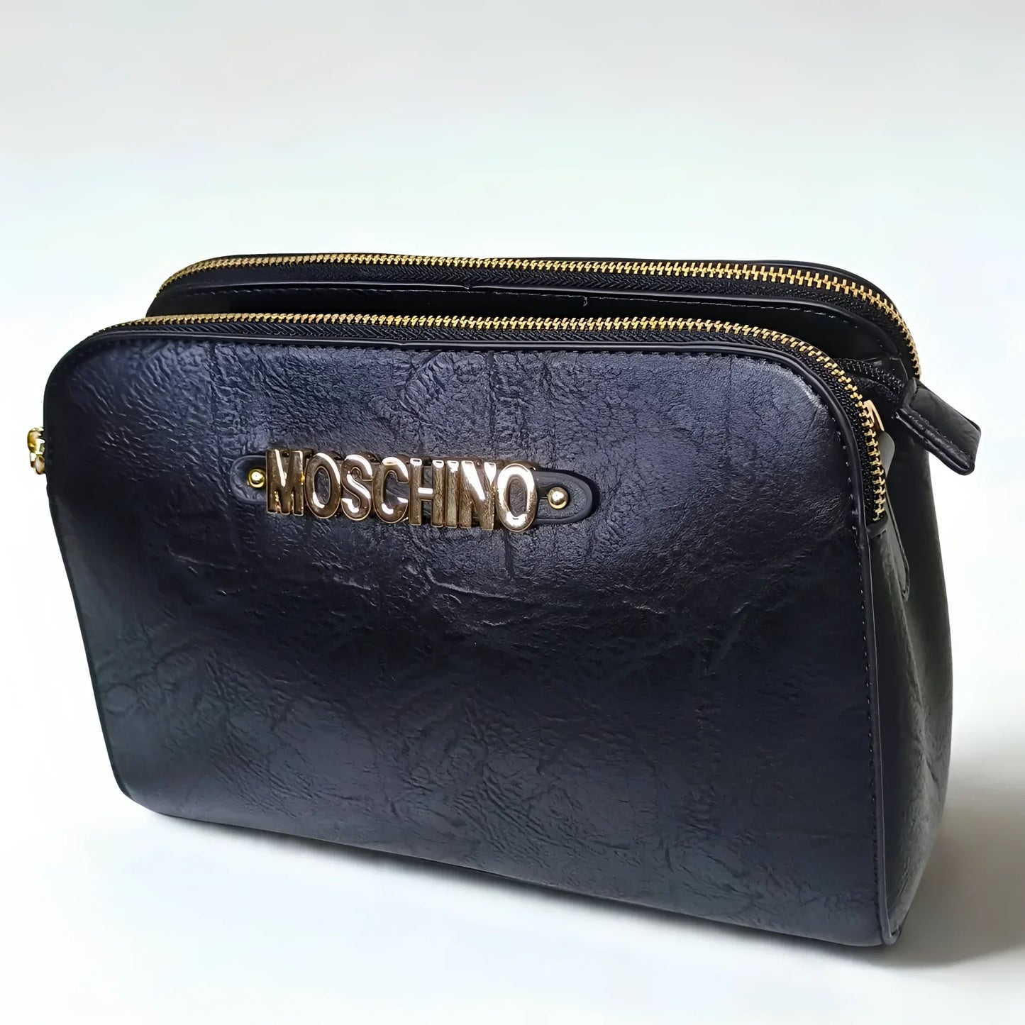 Black leather clutch bag with gold zipper and Moschino logo on a white background