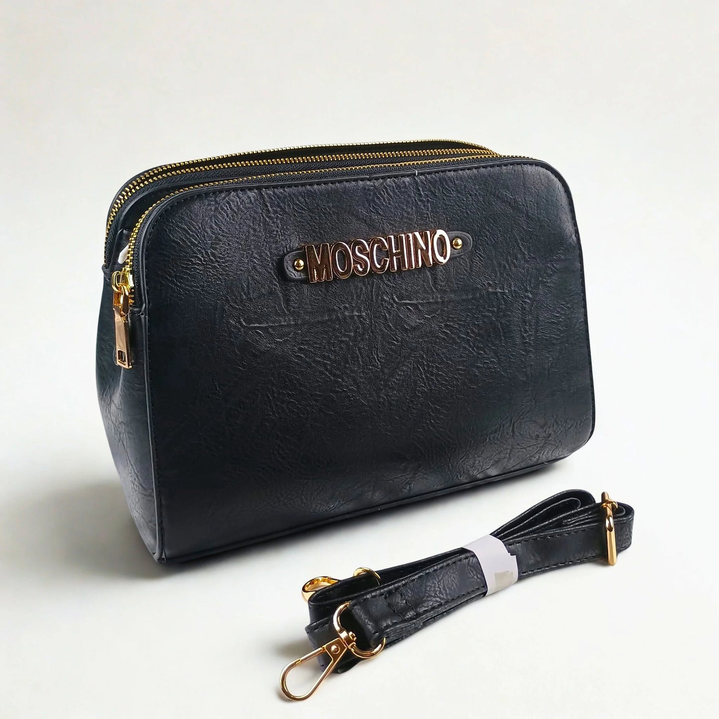Black handbag with gold accents and Moschino logo on a light gray background