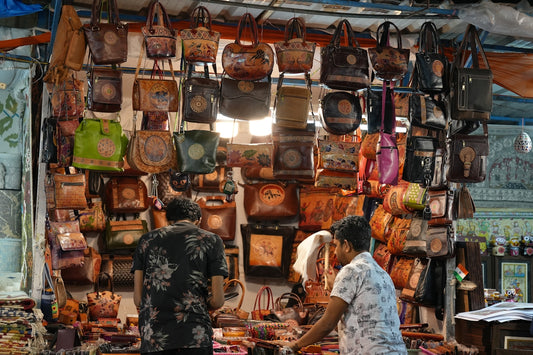 Vendors display many leather bags at a market.