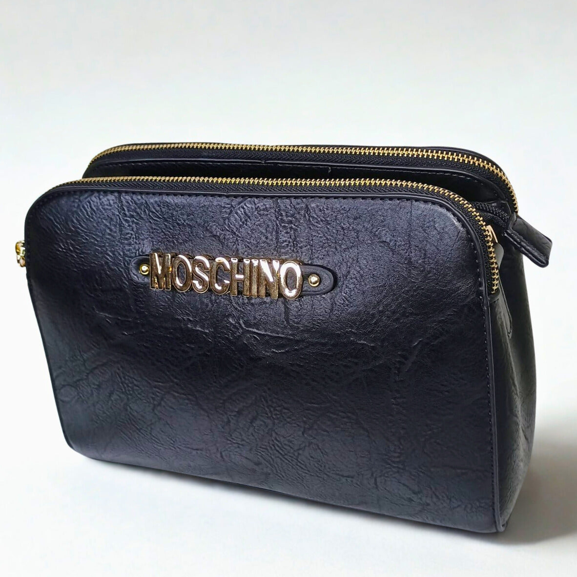 Black leather clutch bag with gold zipper and Moschino logo on a white background