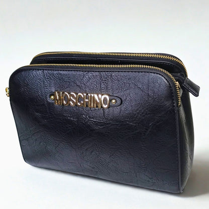 Black leather clutch bag with gold zipper and Moschino logo on a white background