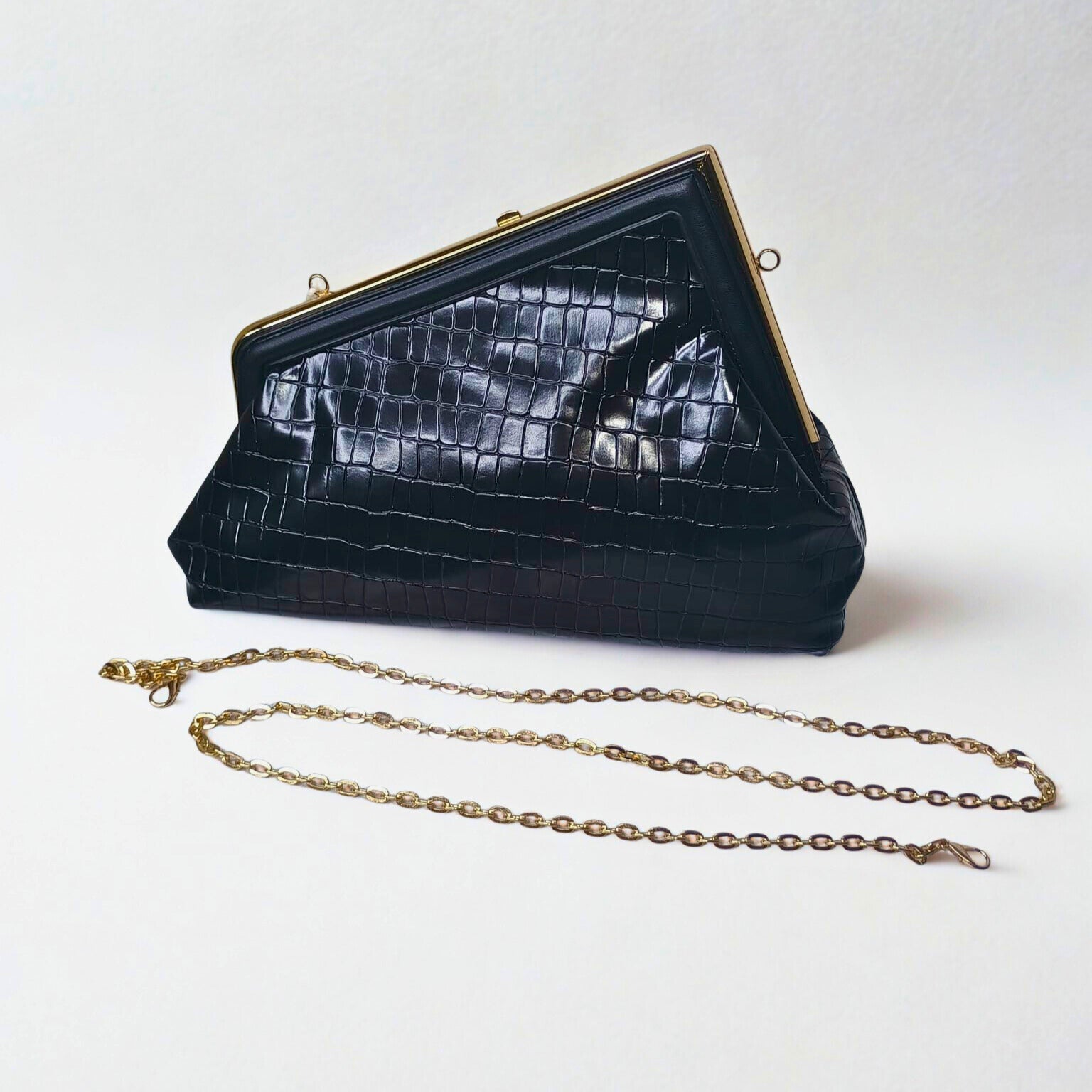 Black crocodile-patterned handbag with gold chain on a white background