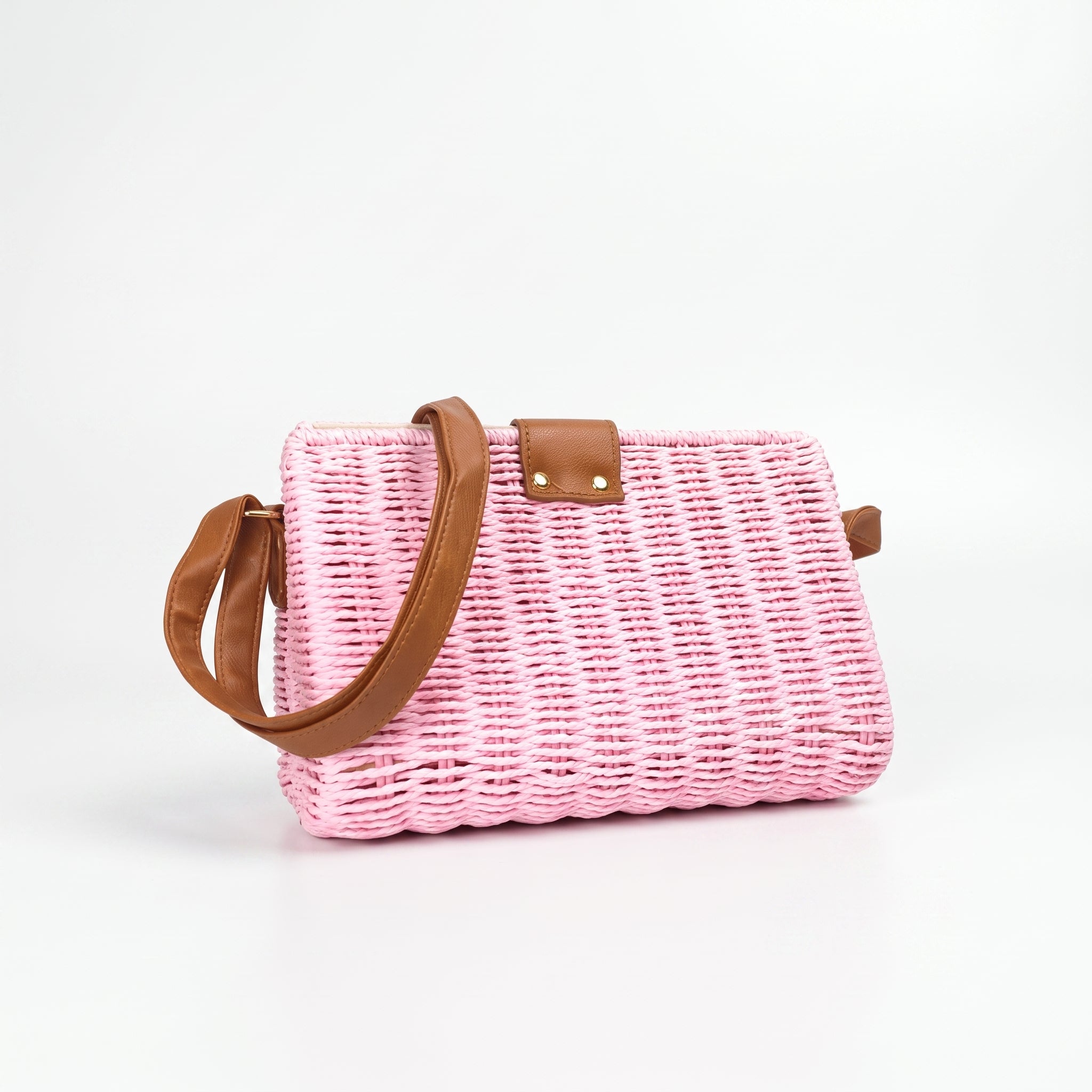 Pink woven handbag with brown leather handle and trim on a white background