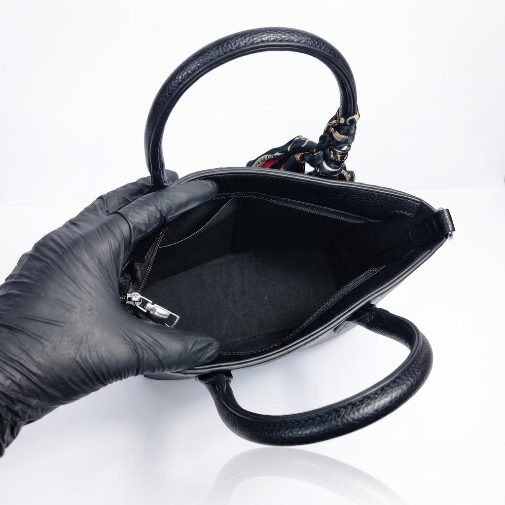 Black handbag held by a gloved hand on a white background