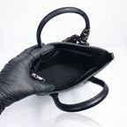 Black handbag held by a gloved hand on a white background