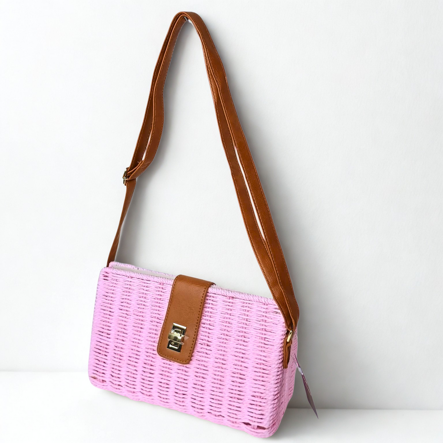 Pink woven handbag with brown leather strap and trim on a white background