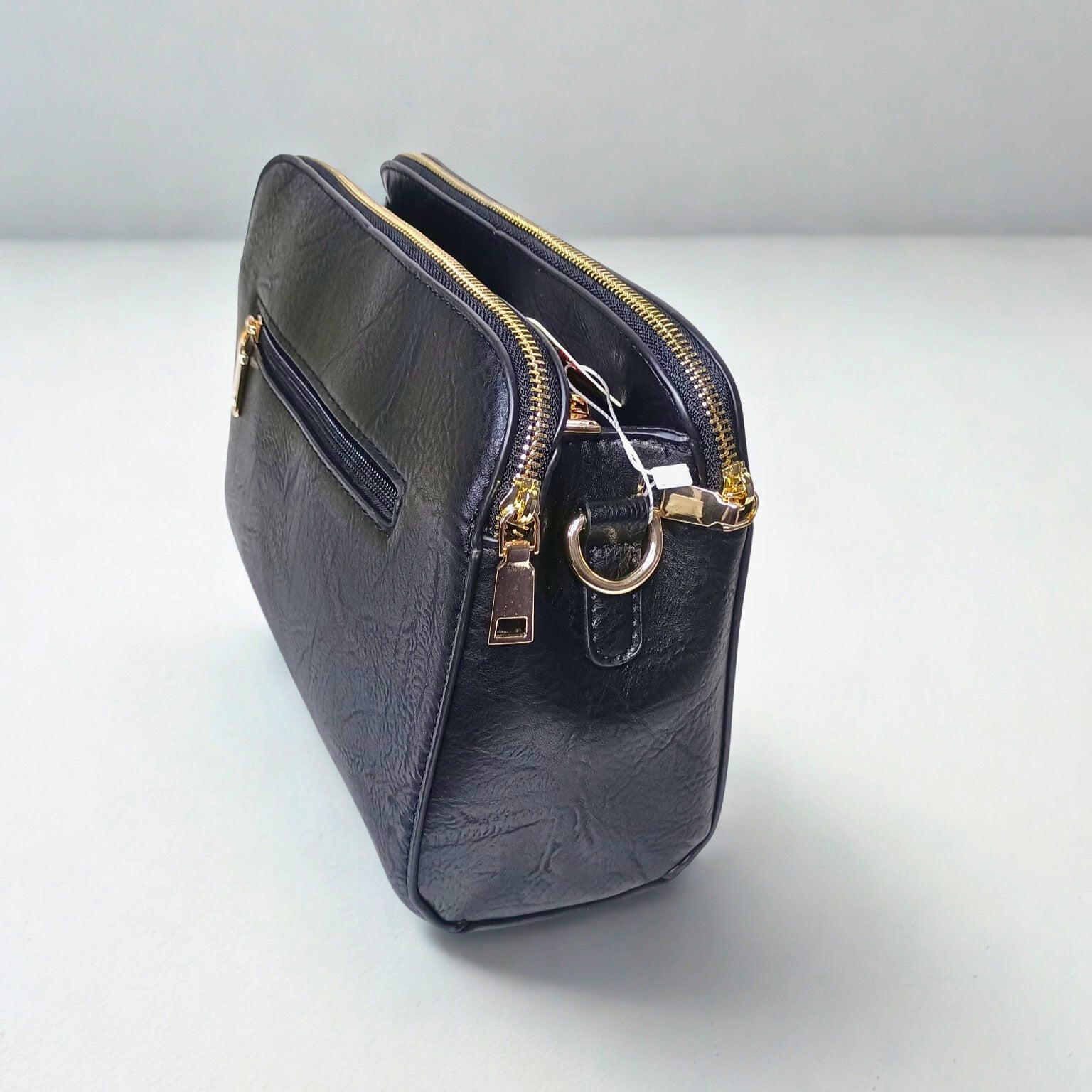 Black handbag with gold zippers and hardware on a light gray background