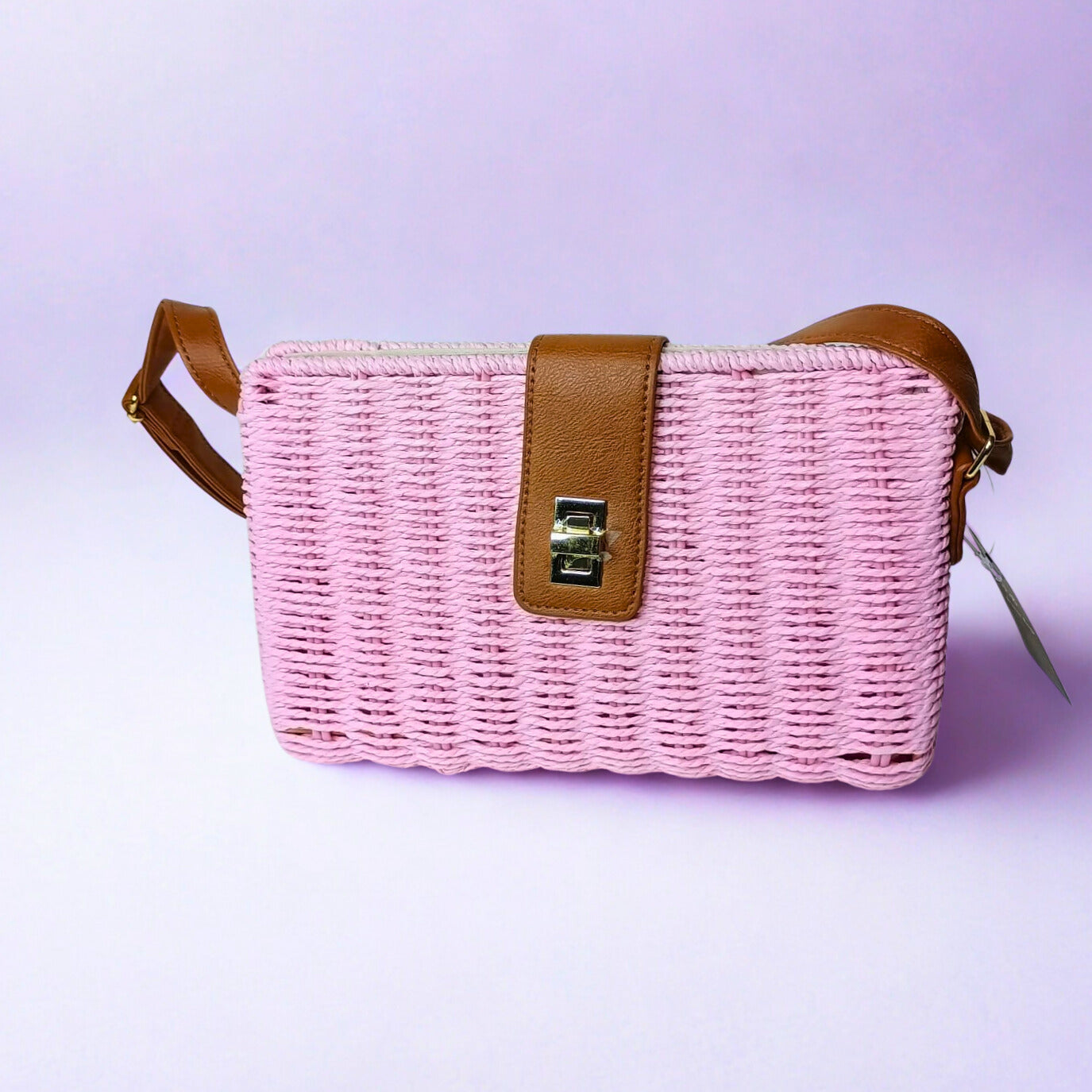 Pink woven handbag with brown leather straps on a light purple background