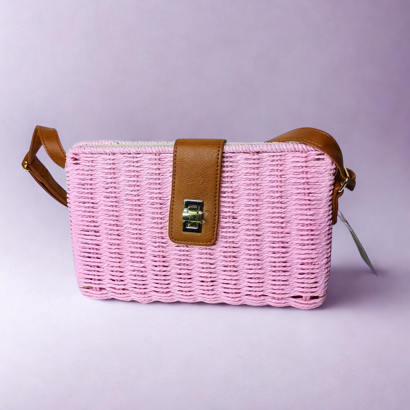 Pink woven handbag with brown leather strap on a light purple background