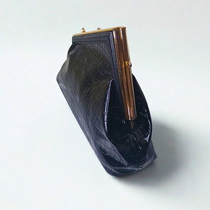 Black textured clutch bag with gold frame on a light gray background