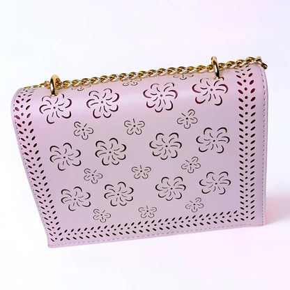 Pink handbag with floral cut-out design and gold chain strap on a white background